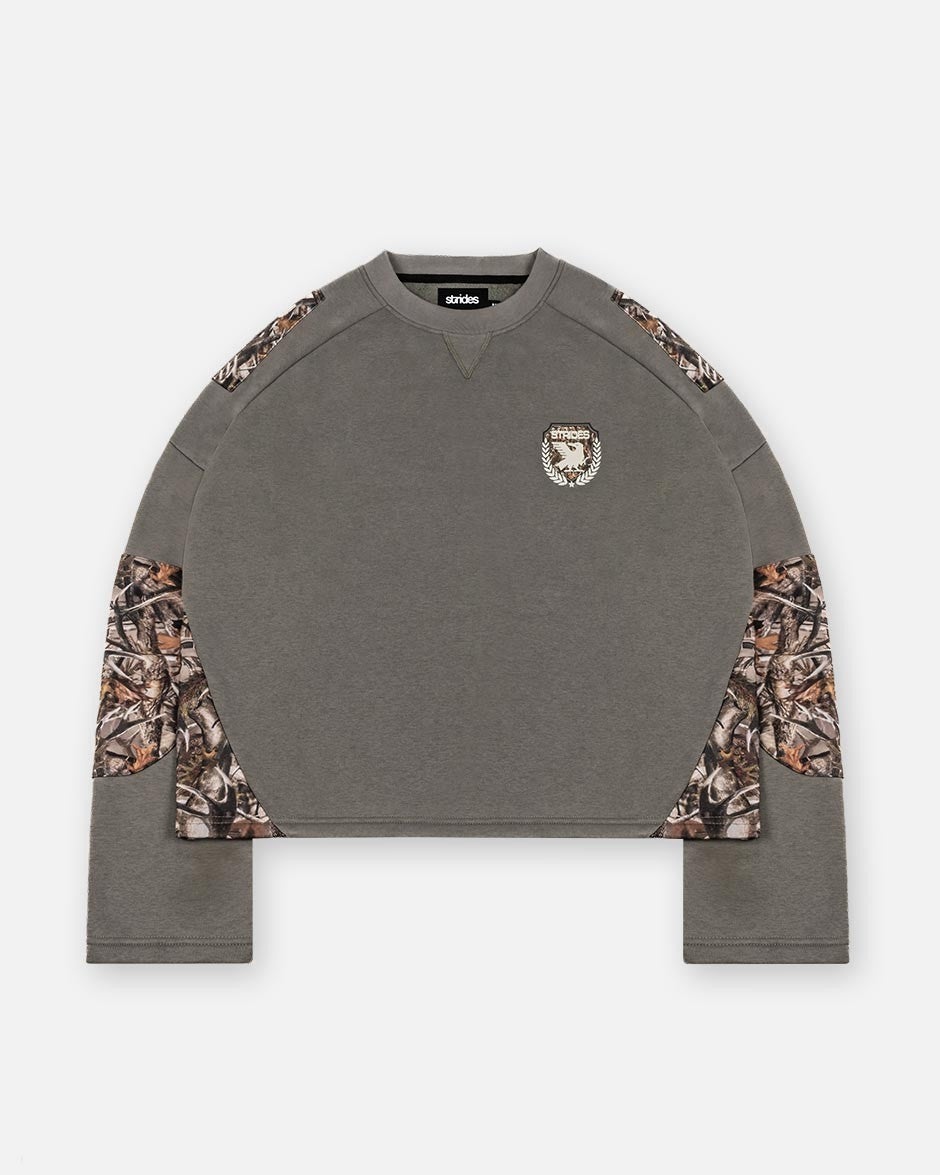 A longsleeve olive green shirt with camouflage patches on the sleeves and a logo print on the chest.