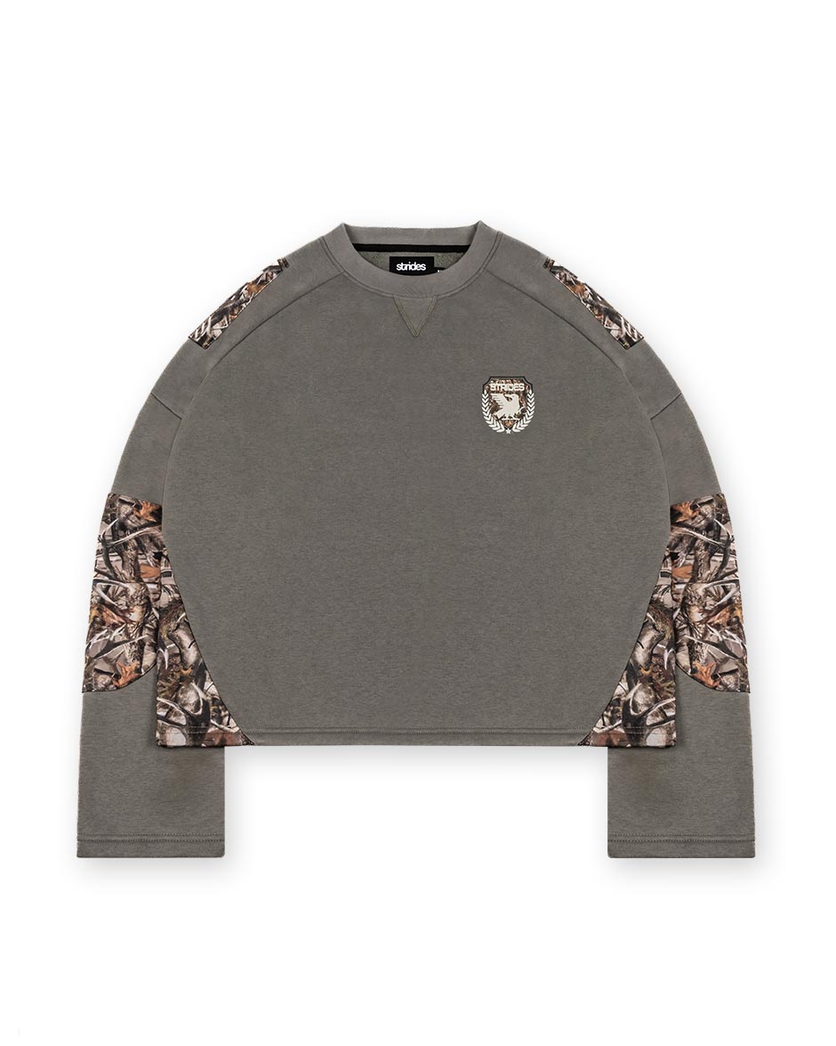 A longsleeve olive green shirt with camouflage patches on the sleeves and a logo print on the chest.