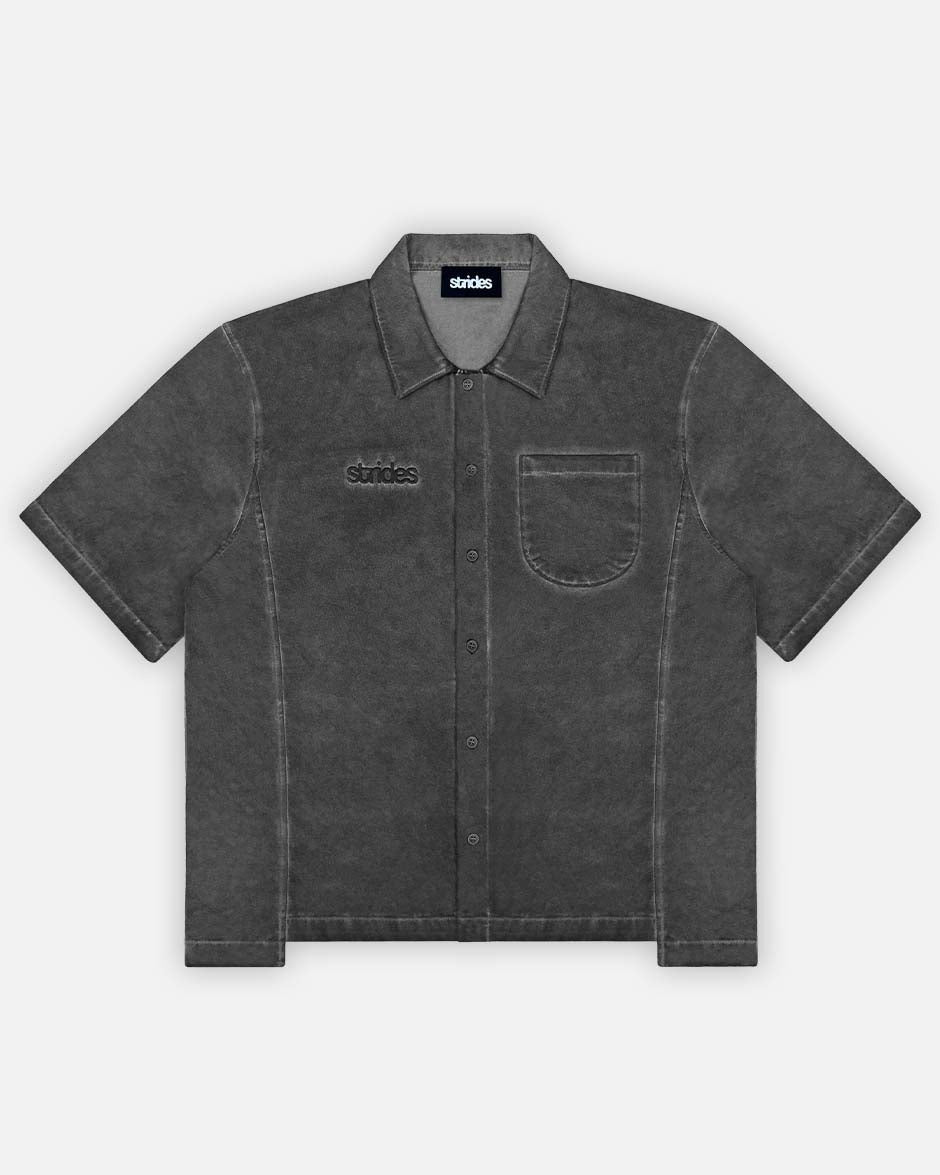 A black, short-sleeved button-up shirt with a collar and front pocket, displaying a washed and slightly distressed look.