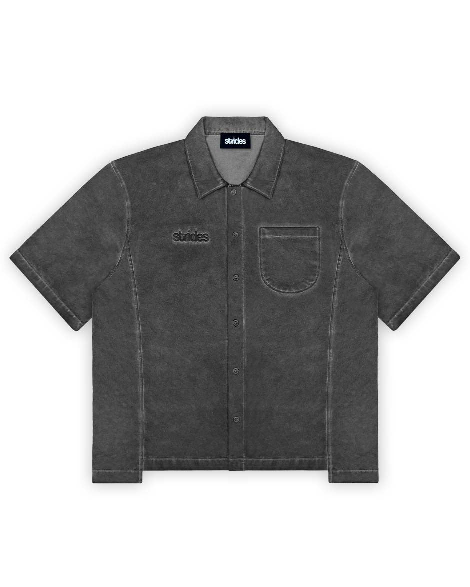 A black, short-sleeved button-up shirt with a collar and front pocket, displaying a washed and slightly distressed look.