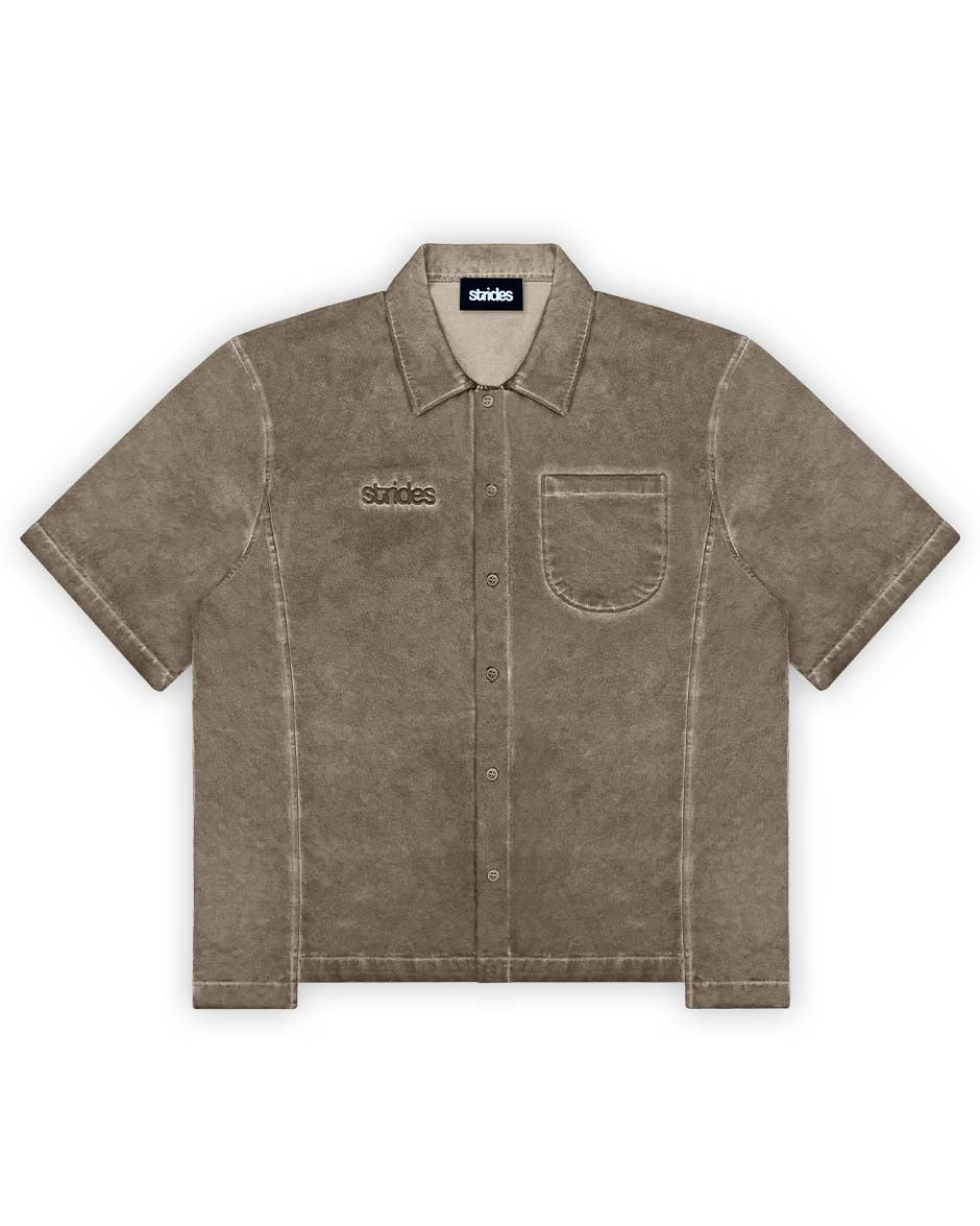 A brown short-sleeved button-up shirt with a collar and front pocket, displaying a washed out look with branding on the chest.