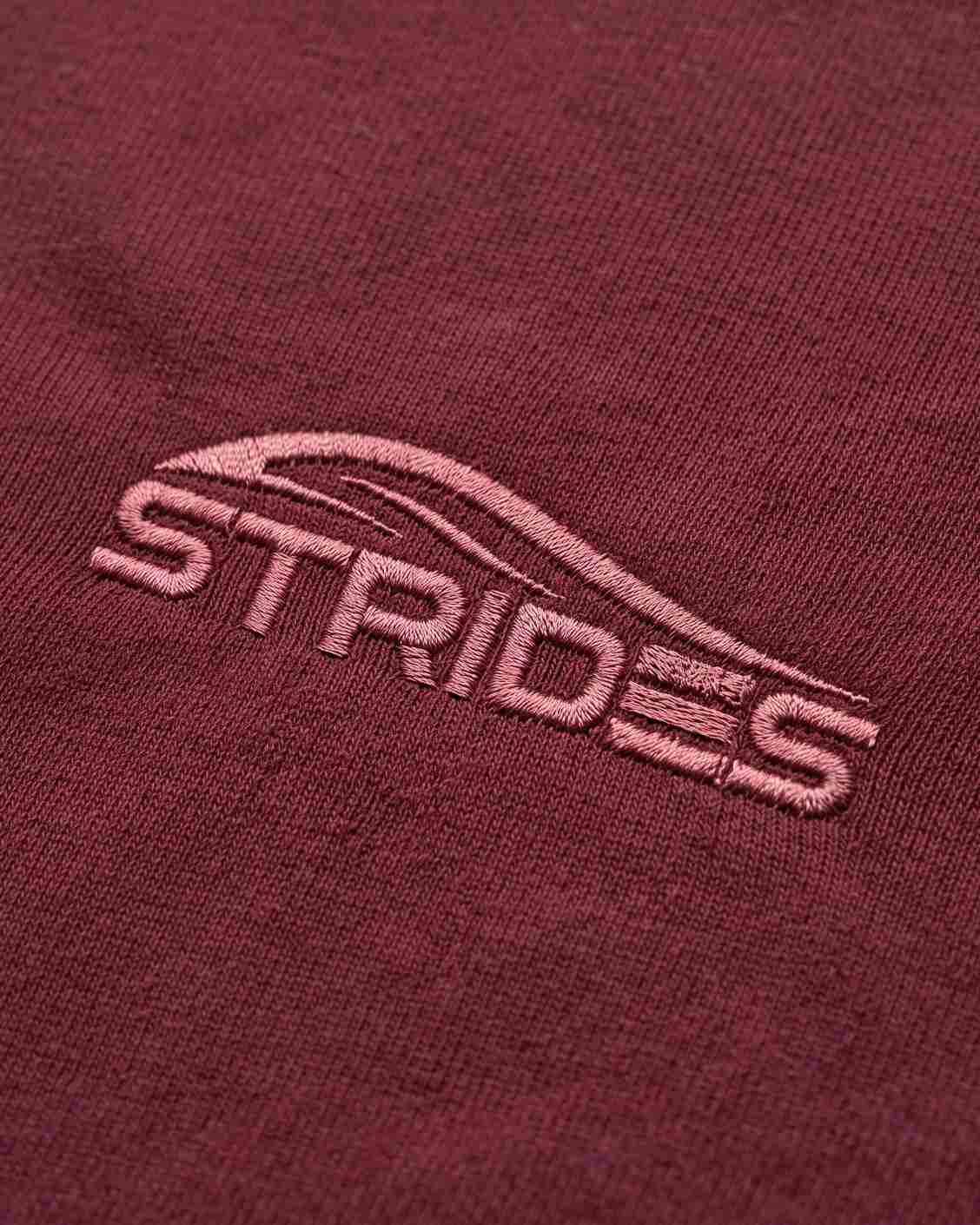 Close-up of the tonal embroidered Strides logo on the bordeaux slim tee