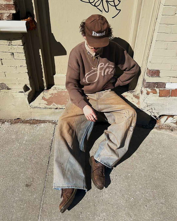 In front of a brick wall, wearing the Echoes Knit Sweater in brown