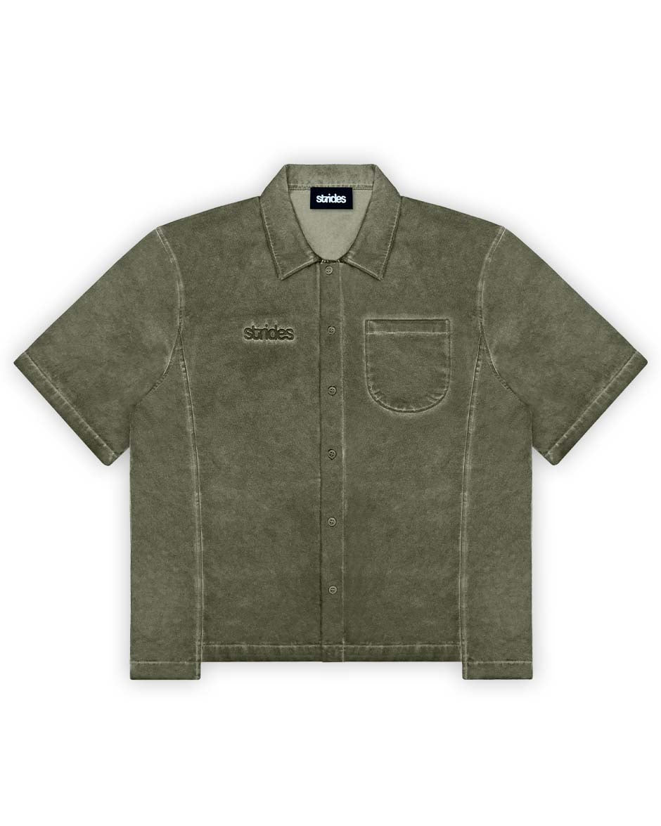 A green cotton shirt with a collar, short sleeves, and front pocket, featuring oil washing and logo embroidery.