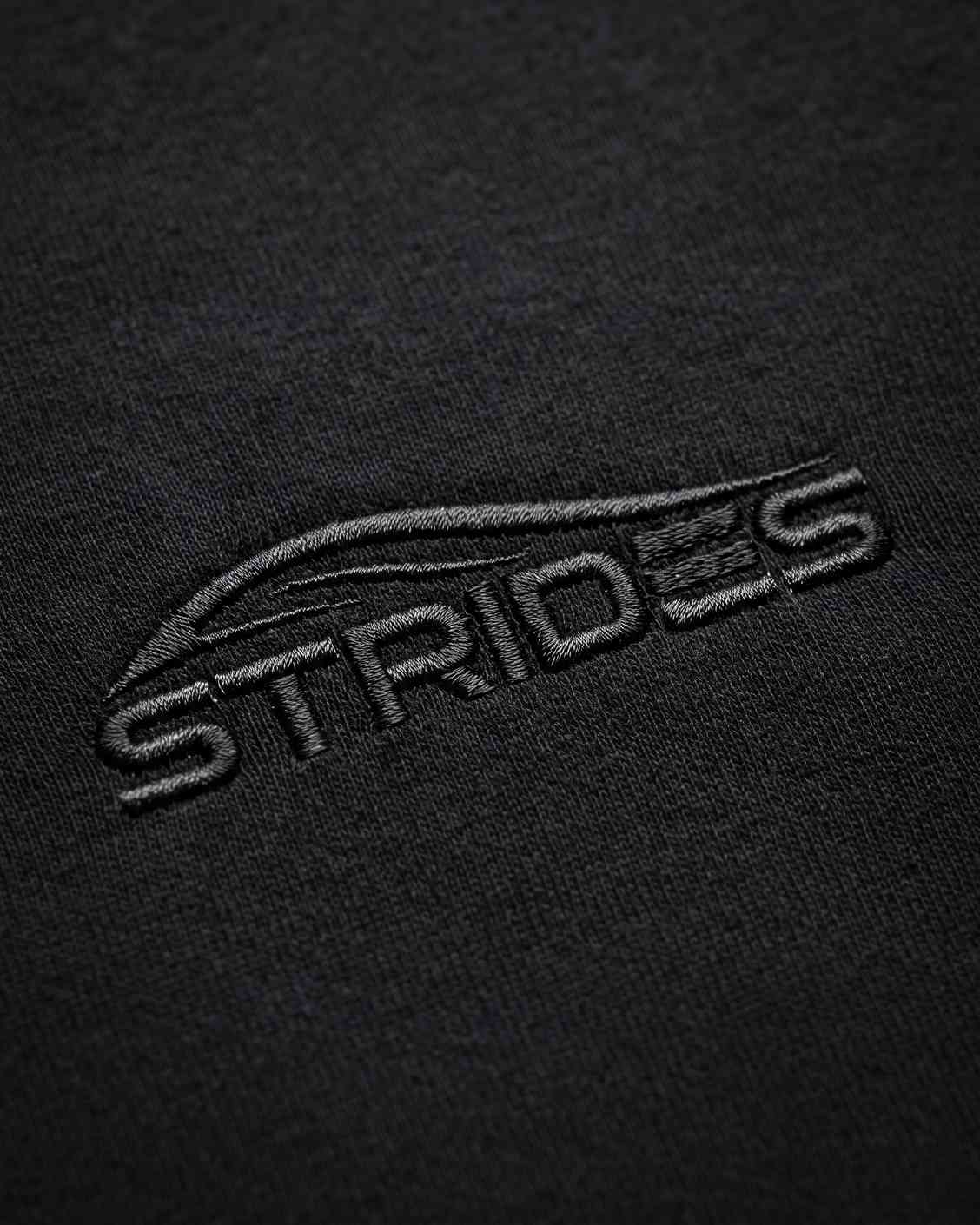 Close-up of the tonal embroidered Strides logo on the black slim tee