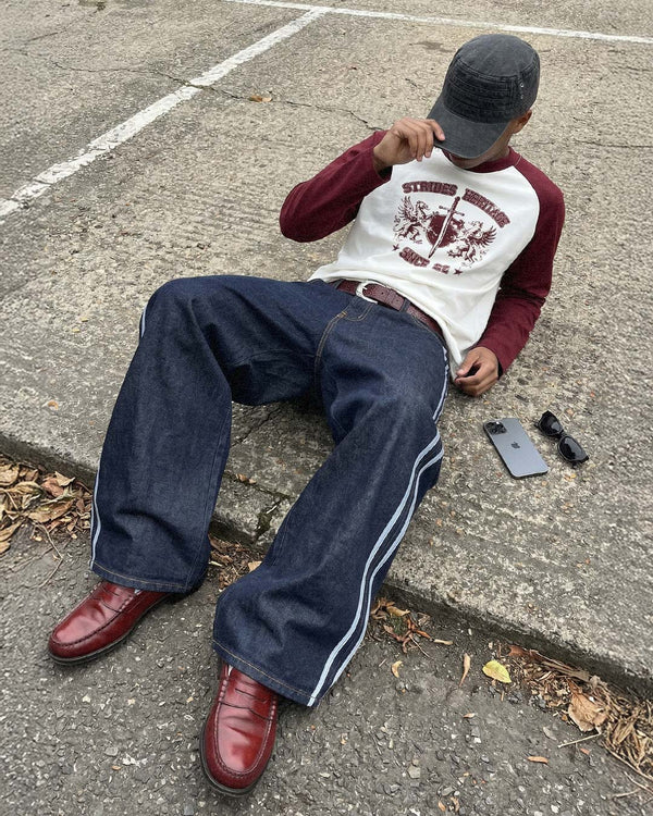 Sitting on a kerb, wearing the burgundy Heritage Raglan Longsleeve