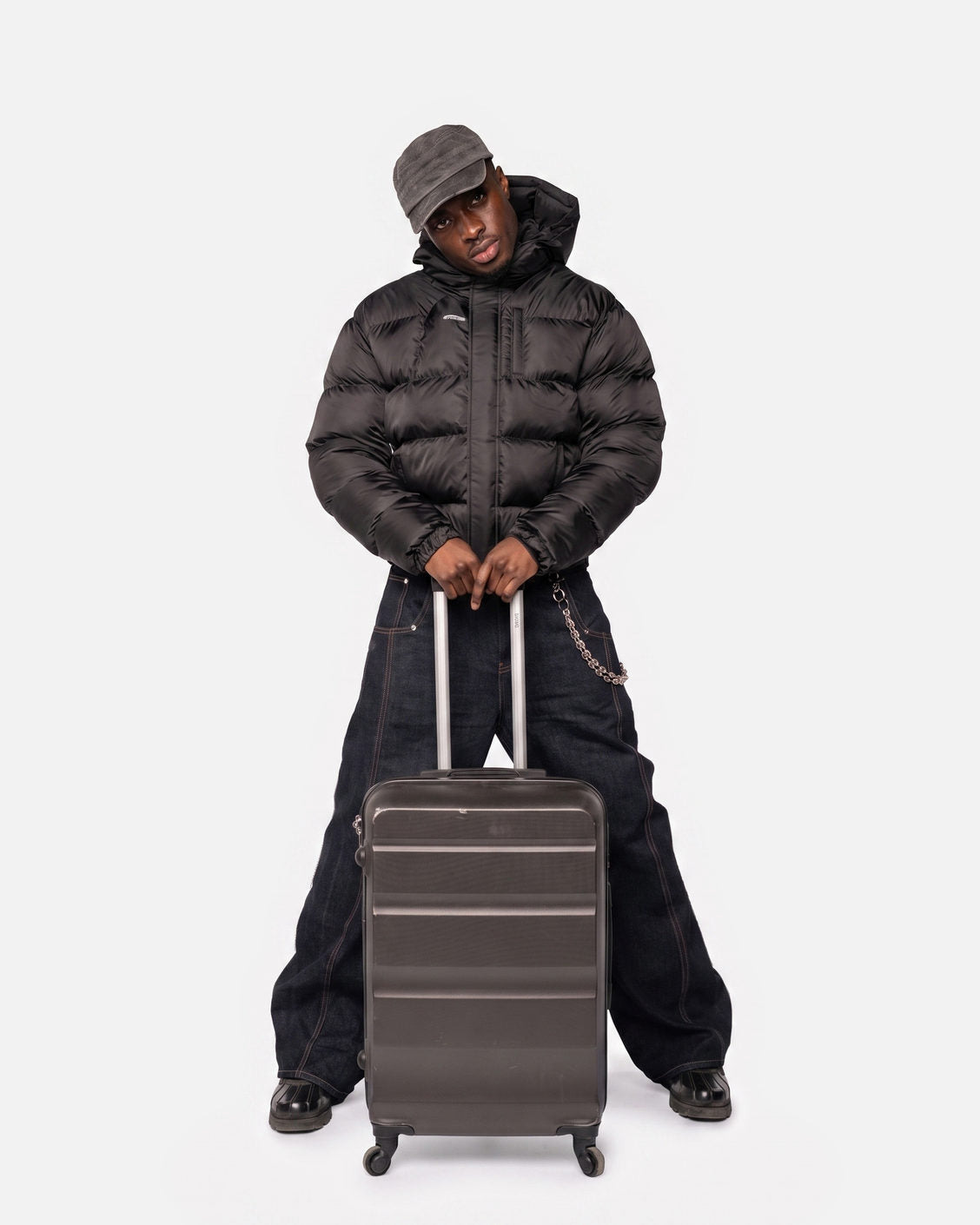 Man wearing the Apex Puffer Black jacket with baggy raw denim jeans and a suitcase